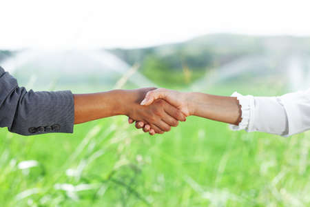 Business women shaking hands in a green field with water sprinkles