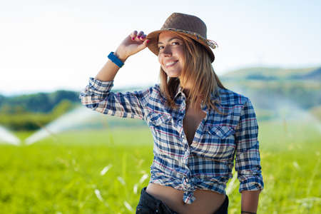 happy girl with hat wearing shirt in a field with water sprinklersの写真素材