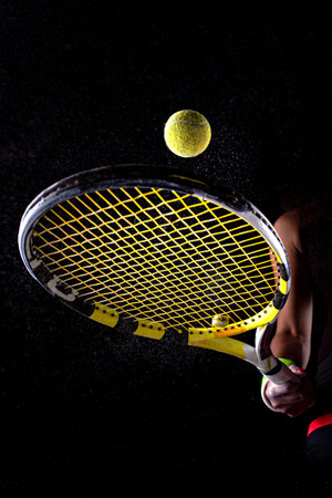 Tennis ball bouncing on racket. Dirt or magnesium dust dots visible in the air. Female player...