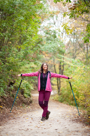 Hiker girl standing on a wide trail in the mountains. Backpacker with pink jacket in a forest....