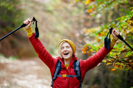 Hiking girl with poles and backpack on a trail. Hands up enjoying in nature. Travel and healthy...
