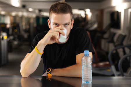 man drinking water while resting in a generic out of focus fitness clubの写真素材