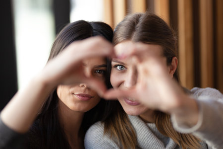 Two lovely girls smiling in a cafe and making a hearth shape with their hands.の写真素材