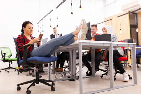 Group of multiethnic colleagues working on desktop computers in a modern office space. Girl resting with feet on tableの写真素材