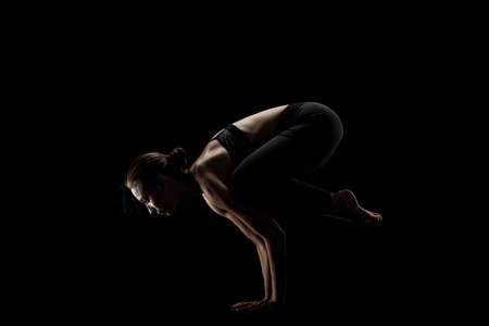 cute caucasian girl exercising yoga poses against dark backgroung. side lit silhouette.の写真素材