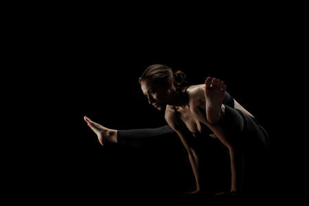 cute caucasian girl exercising yoga poses against dark backgroung. side lit silhouette.の写真素材