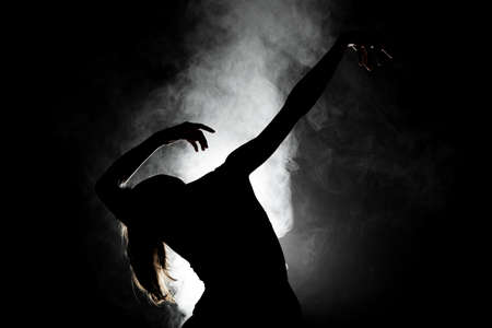 silhouette modern ballet dancer posing on dark background with smoke