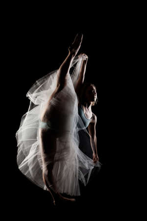 ballerina with a white dress and black top posing on black backgroundの写真素材