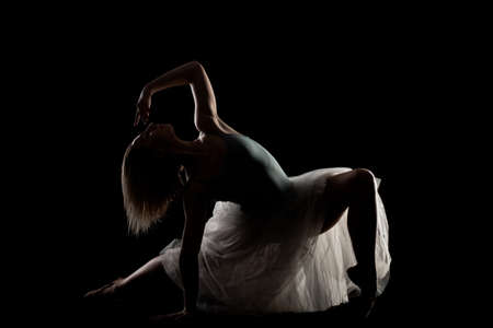 ballerina with a white dress and black top posing on black background. side lit silhouetteの写真素材