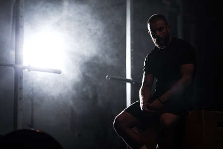Silhouette of a muscular athlete posing in interior with weightlifting equipment. Smoke background.の写真素材