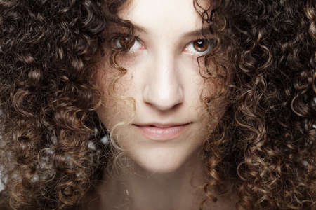 Beautiful brunette girl with long curly hair. Closeup studio portrait. Serious face expression.の写真素材