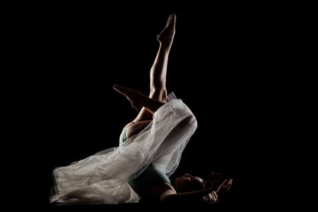 ballerina with a white dress and black top posing on black background. side lit silhouetteの写真素材