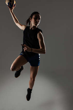 Handball player posing on gray background. Girl jumping with ball.の写真素材
