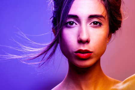 Beautiful brunette girl studio portrait. Neon lights. Serious face expression.