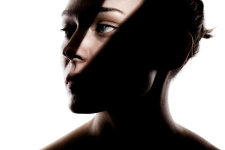 Fashionable studio portrait of a cute girl. Silhouette of a beautiful young woman with hard shadows on her face against white backgroung.の写真素材
