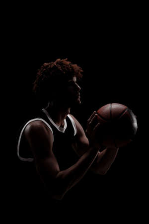 Professional basketball player holding a ball against black background. Serious concentrated african american man in sports uniform.の写真素材