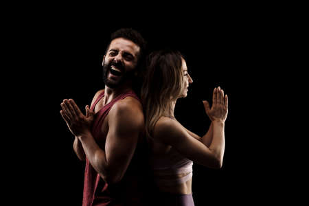 Fit couple posing together. Girl praying boy having fun. Side lit silhouettes on black background.の写真素材