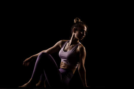 Fit girl practicing yoga in a studio. Half silhouette side lit fitness model