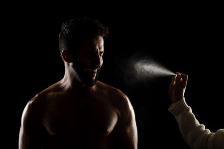 Side lit muscular Caucasian man silhouette. Athlete being sprayed with water or perfume against black background.の写真素材