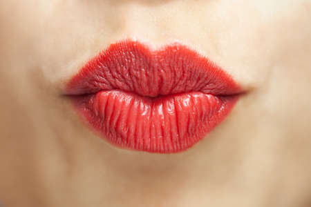 Close up abstract portrait of a beautiful caucasian girl. Lips blowing a kiss with red lipstick.の写真素材