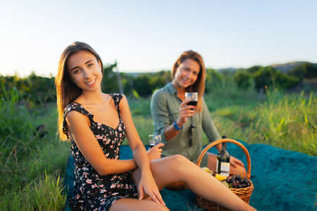 Beautiful girls tasting wine in a field near vineyard field. Celebrating successful harvest season. Couple having a romantic date. Rural tourism concept..の写真素材