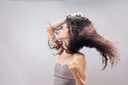 Beautiful brunette girl with long curly hair in the air, studio portrait. Serious face expression.の写真素材