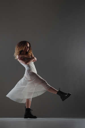 Girl with curly hair making ballet poses. Ballerina in white dress and black boots.の写真素材