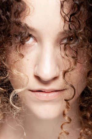 Beautiful brunette girl with long curly hair. Closeup studio portrait. Serious face expression.の写真素材