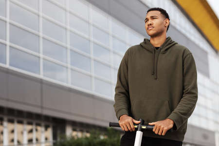young african american man in casual clothing posing on electric scooterの写真素材