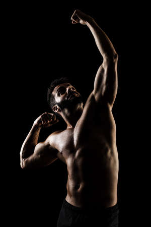 Side lit muscular Caucasian man silhouette. Athlete posing against black background.