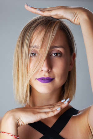 Beautiful blond girl with purple lipstick studio portrait. Hand gestures.の写真素材
