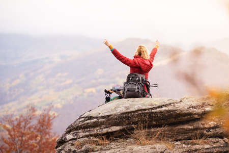 Hiker girl sitting on a rock in the mountains. Enjoying the view with hands up. Travel and healthy lifestyle outdoors in fall seasonの写真素材