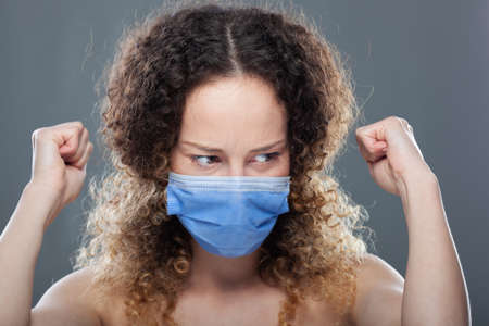 Girl with curly hair wearing medical face mask to protect herself viruses, polution or dust. Studio...