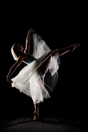 ballerina with a white dress and black top posing on black backgroundの写真素材