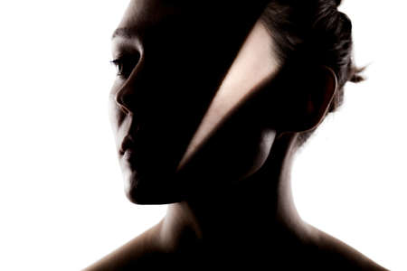 Fashionable studio portrait of a cute girl. Silhouette of a beautiful young woman with hard shadows on her face against white backgroung.の写真素材