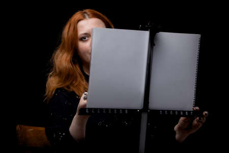 Red hair woman painting. Portrait of an artist against black background.の写真素材