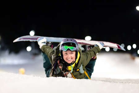 Snowboarder girl posing on slopes. Night skiing in winter resort.