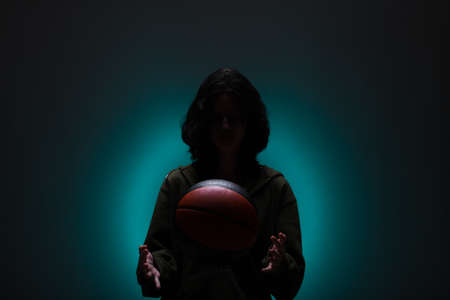 Teenage girl with basketball. Silhouette studio portrait with neon blue colored background.の写真素材