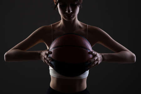 Teenage girl with basketball. Side lit studio portrait against dark background.の写真素材