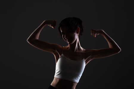 Side lit half silhouette portrait of a beautiful teenage girl in studio against dark background.の写真素材