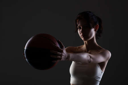 Teenage girl with basketball. Side lit studio portrait against dark background.の写真素材