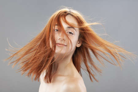 Beautiful dark burnt orange windy hair girl smiling. Studio portrait with happy face expression against gray background.の写真素材