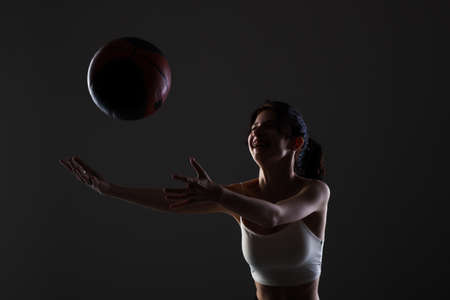 Teenage girl with basketball. Side lit studio portrait against dark background.の写真素材