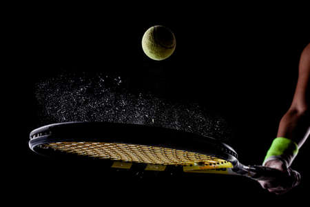 Tennis ball bouncing on racket. Dirt or magnesium dust dots visible in the air.の写真素材
