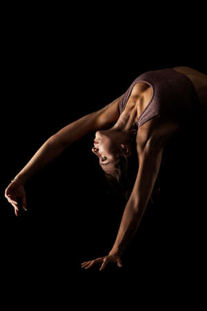 Fit woman practicing yoga poses. Side lit half silhouette girl doing exercise in studio against black background.の写真素材