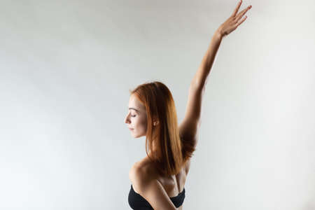 Beautiful girl with burnt orange hair stretching and making ballet pose. Studio portrait on gray background.の写真素材