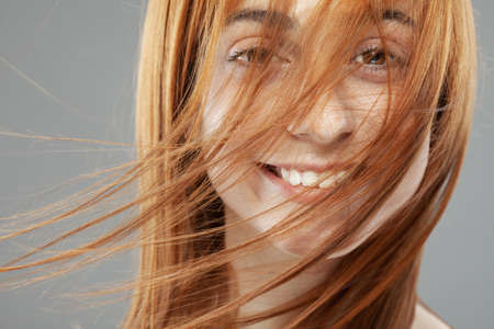 Beautiful dark burnt orange windy hair girl smiling. Studio portrait with happy face expression against gray background.の写真素材