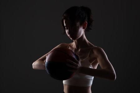 Teenage girl with basketball. Side lit studio portrait against dark background.の写真素材