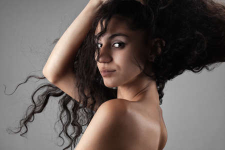 Beautiful brunette girl with long curly hair in the air, studio portrait on dark gray background.の写真素材