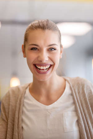 Portrait of a beautiful girl with big smile and very positive face expression looking at camera in an office space.の写真素材